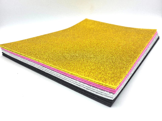 Stack of glittery cardstock sheets in gold, pink, and black on a white background