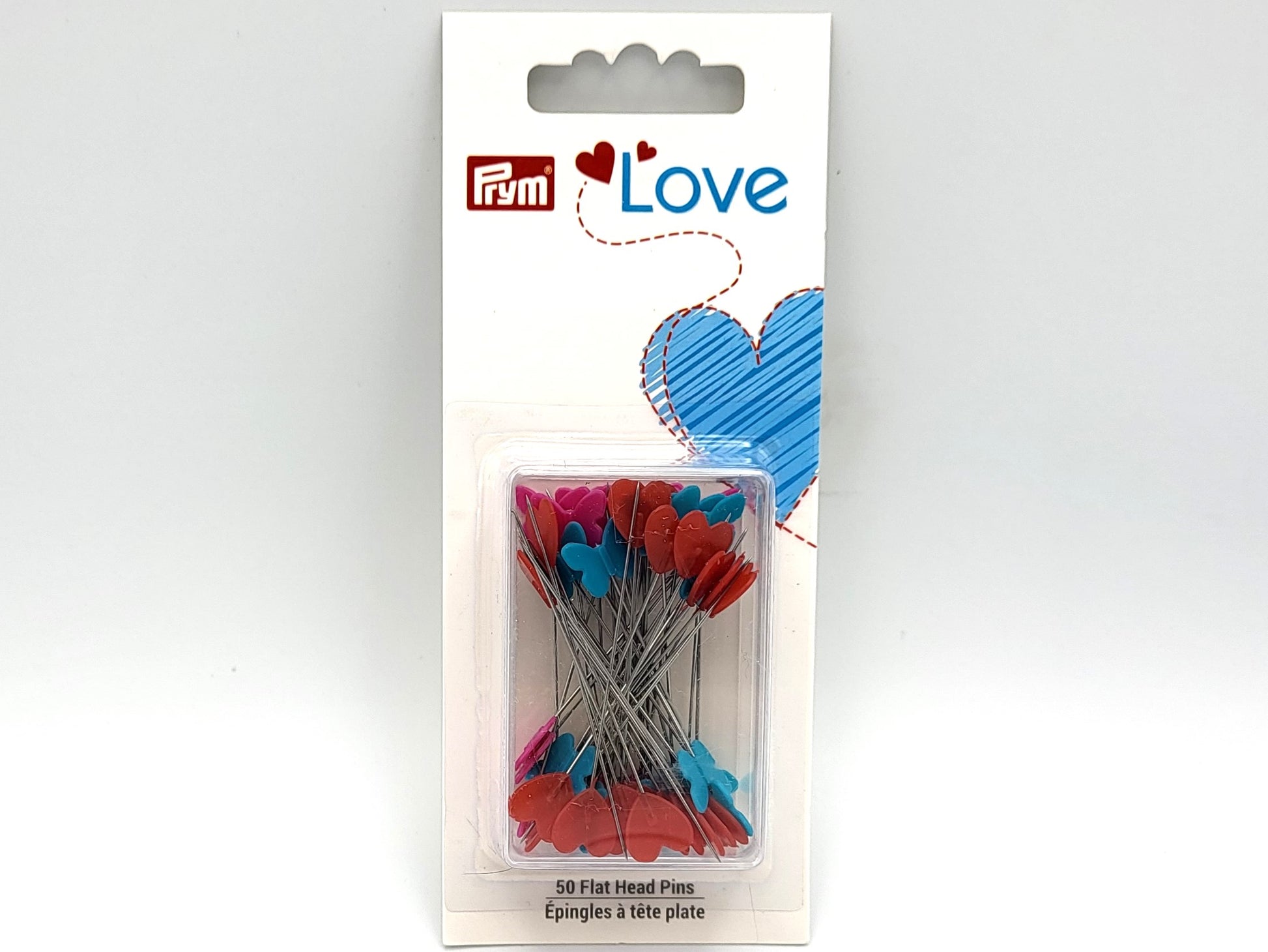 Packaging of Dritz Prym Love flat head pins with turquoise and pink butterflies and red hearts on them, displayed in a clear plastic box with a white background.