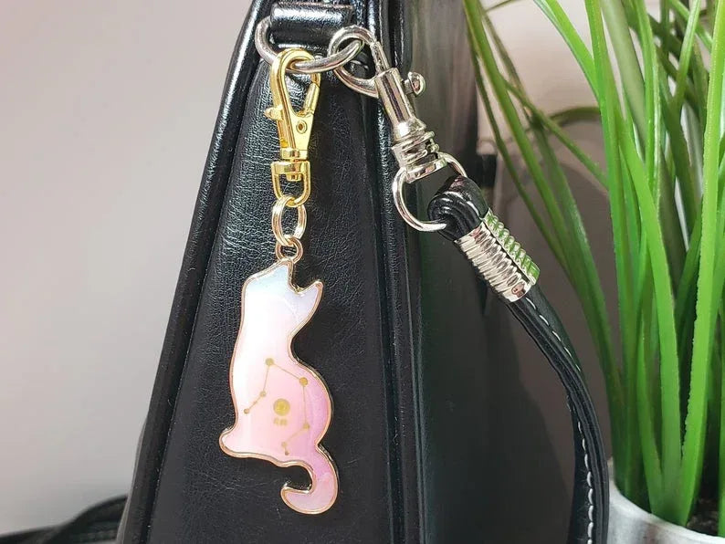 Pink cat-shaped keychain attached to a black bag with a plant in the background