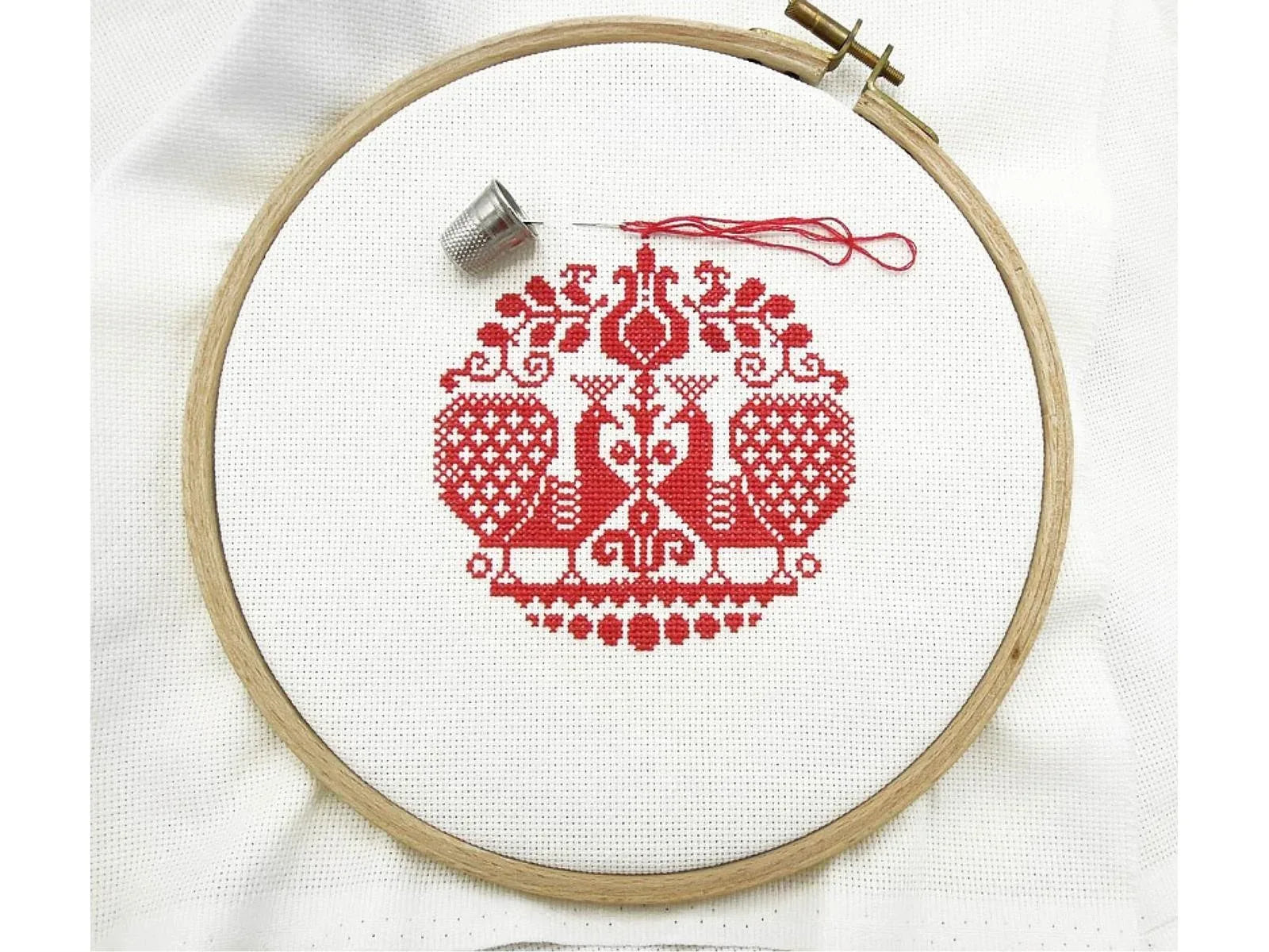Embroidery hoop with red cross-stitched design on white fabric