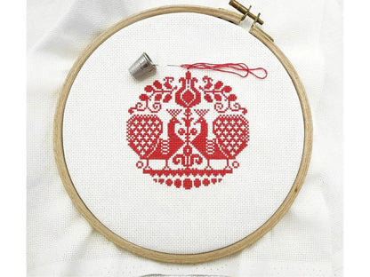 Embroidery hoop with red cross-stitched design on white fabric