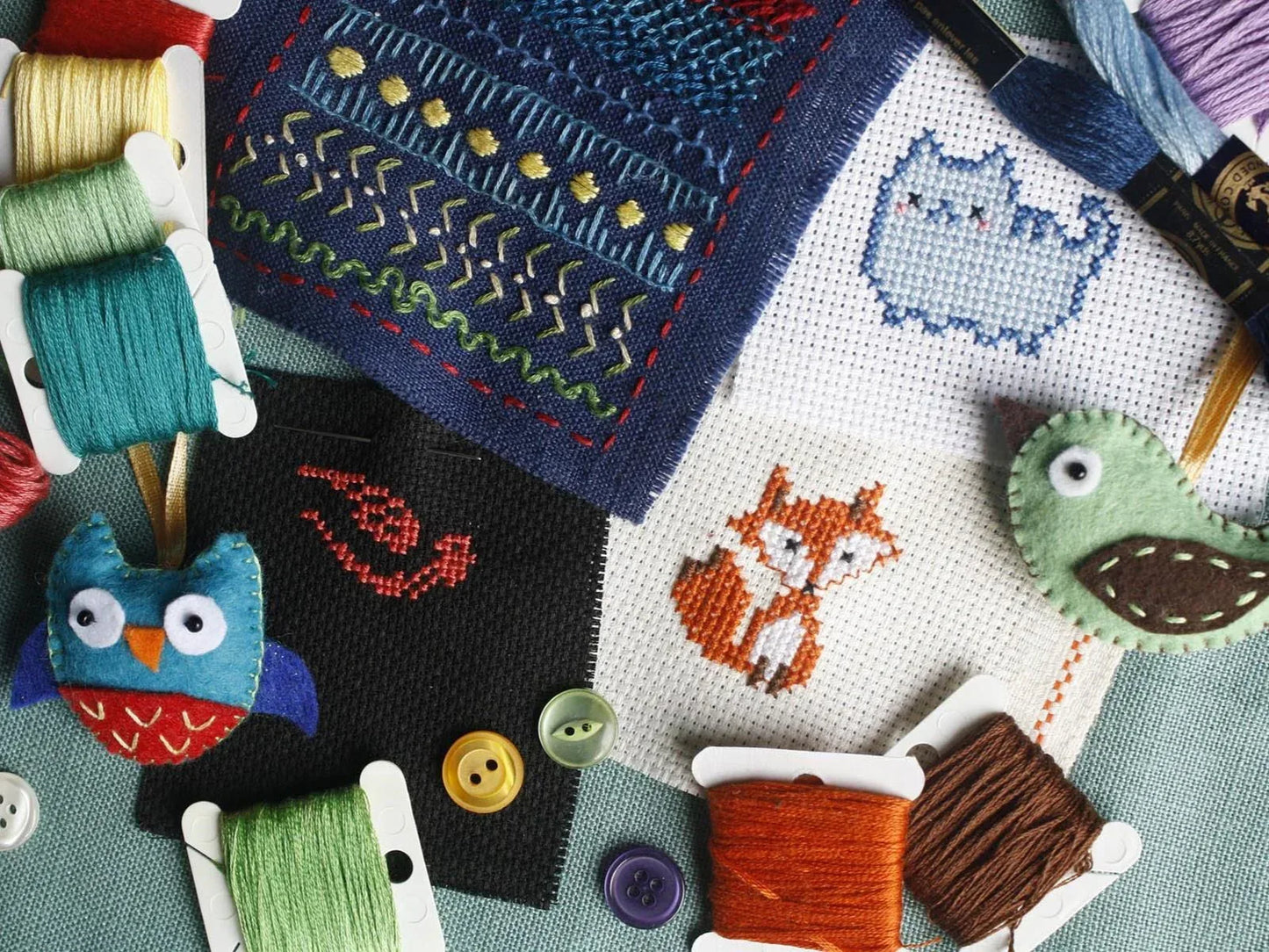 Cross-stitched pieces with animals and buttons, surrounded by spools of thread.