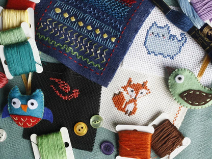 Cross-stitched pieces with animals and buttons, surrounded by spools of thread.
