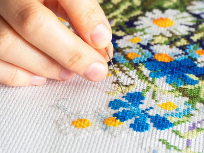 Hand holding a needle over a cross-stitched floral pattern