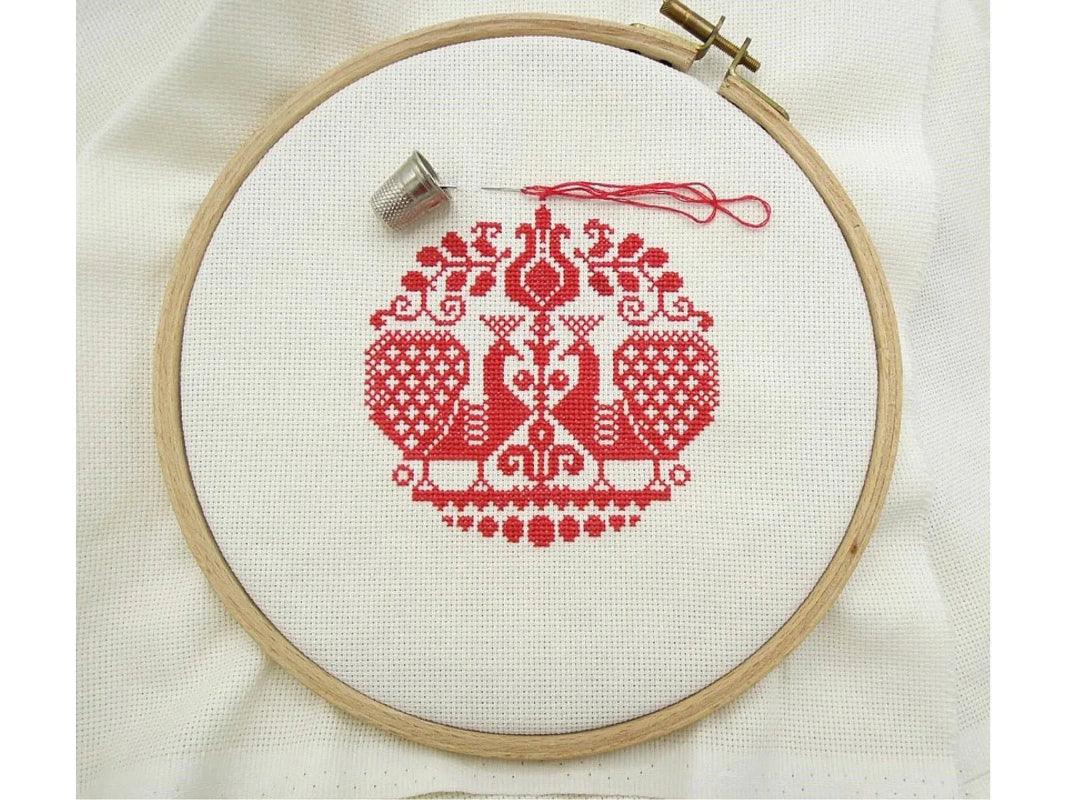 Embroidery hoop with red cross-stitched design on white fabric