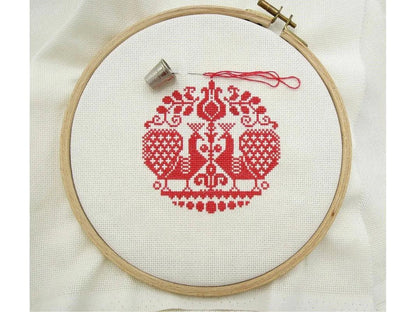 Embroidery hoop with red cross-stitched design on white fabric