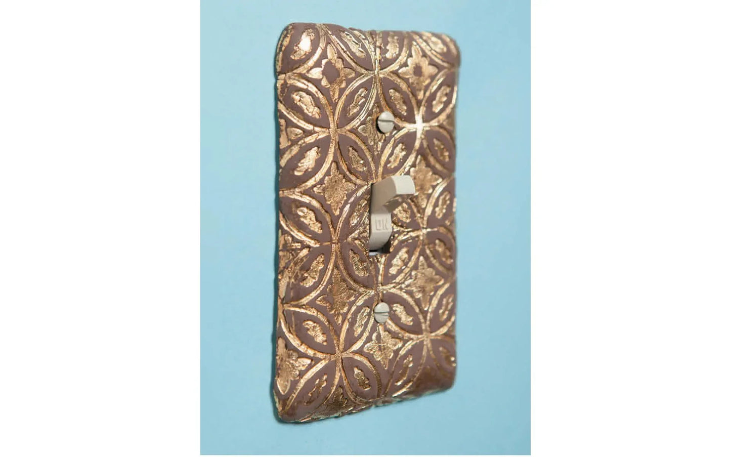 Decorative metal light switch cover with intricate patterns on a blue background
