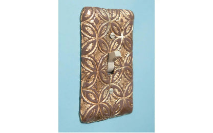 Decorative metal light switch cover with intricate patterns on a blue background