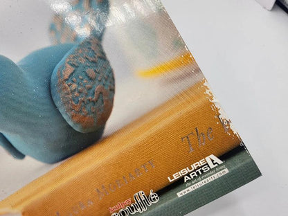 Close-up of a Leisure Arts craft kit with a blue plastic object and clear packaging.