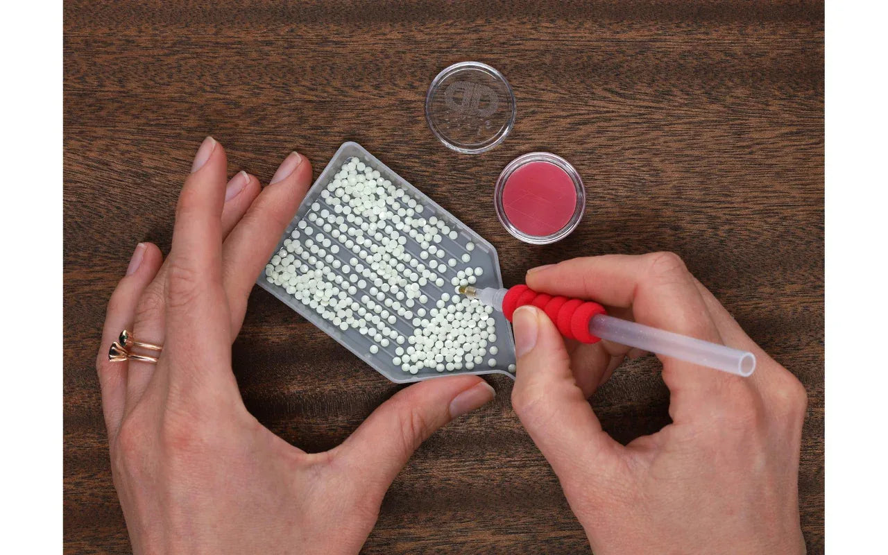 Person using a small tool to work with beads on a wooden surface