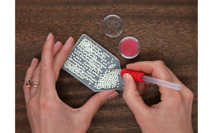 Person using a small tool to work with beads on a wooden surface