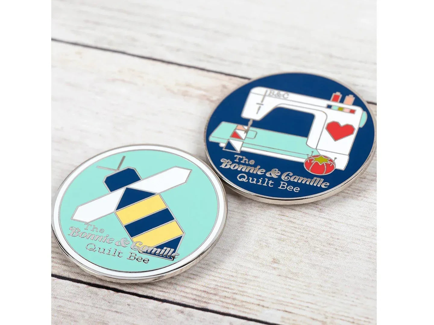 Two round pins with sewing-themed designs on a wooden surface