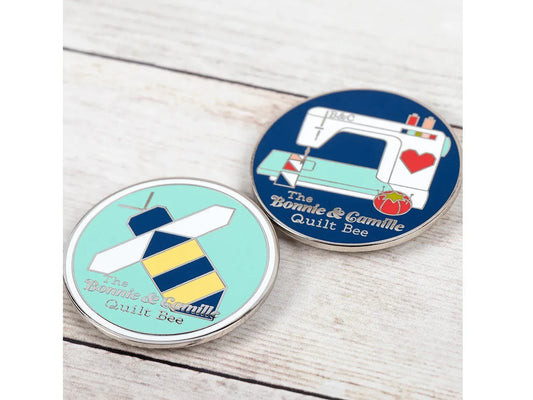 Two round pins with sewing-themed designs on a wooden surface