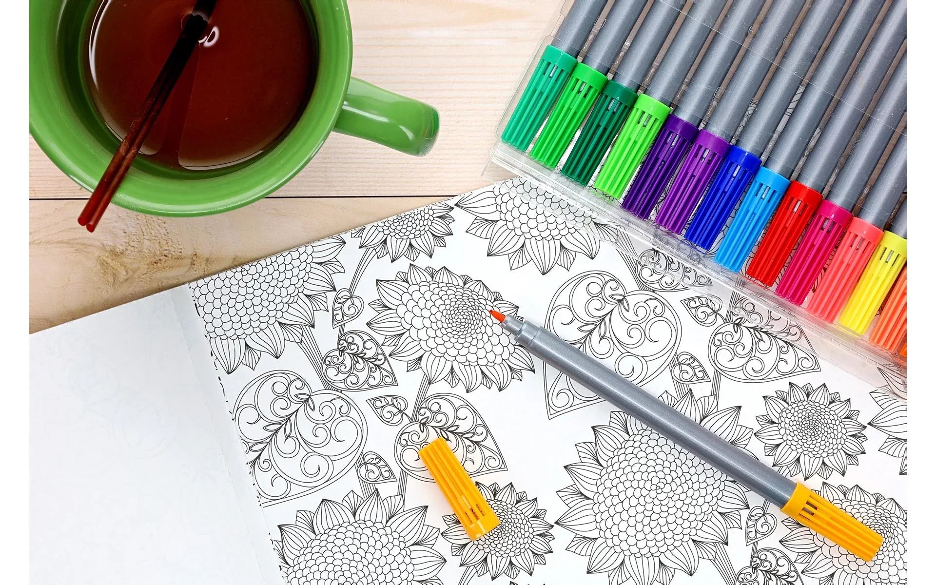 Coloring book with intricate designs, colored pencils, and a cup of tea on a wooden surface.