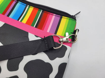 Colorful striped pouch with a black strap and cow print pattern on a white background