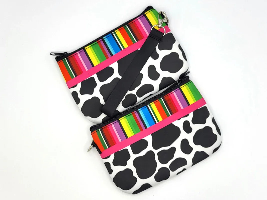 Two cow print pouches with colorful striped zippers on a white background