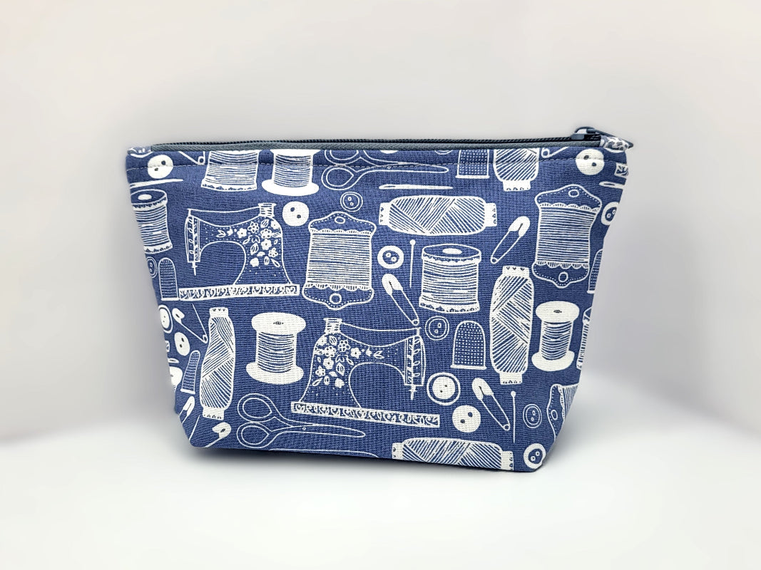 Blue pouch with white sewing-themed pattern on a white background