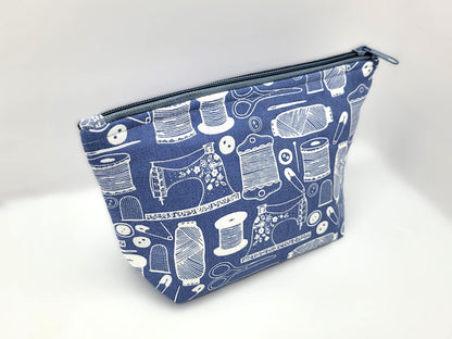 Blue pouch with white sewing-themed pattern on a white background