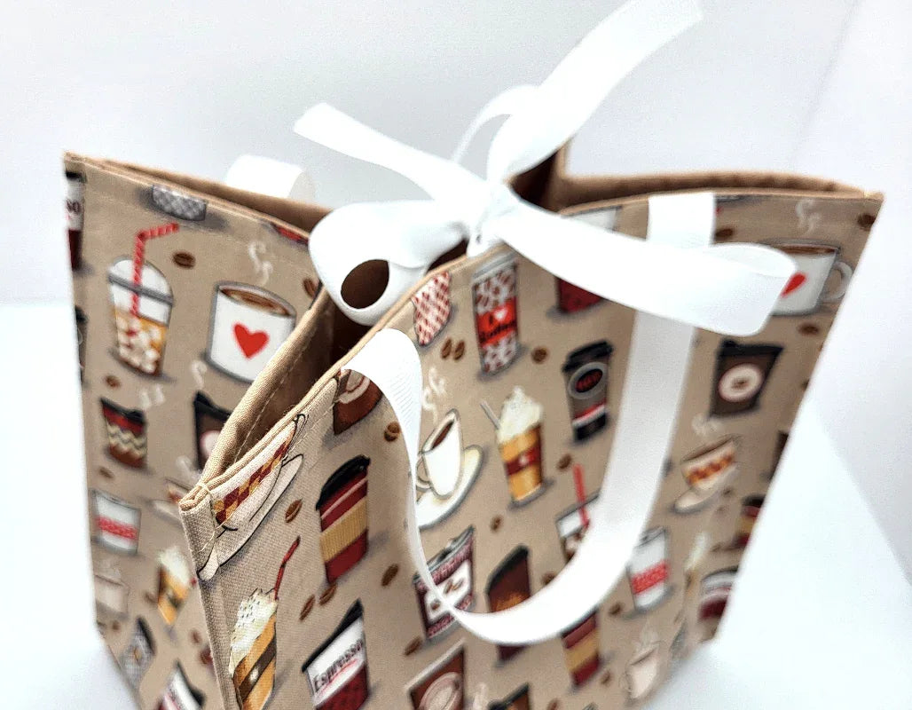 Fabric bag with coffee-themed design and white ribbon on a light background