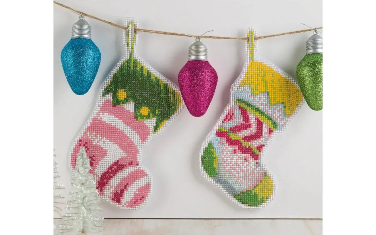 Cross-stitched stockings with floral patterns hanging on a string with decorative lights.