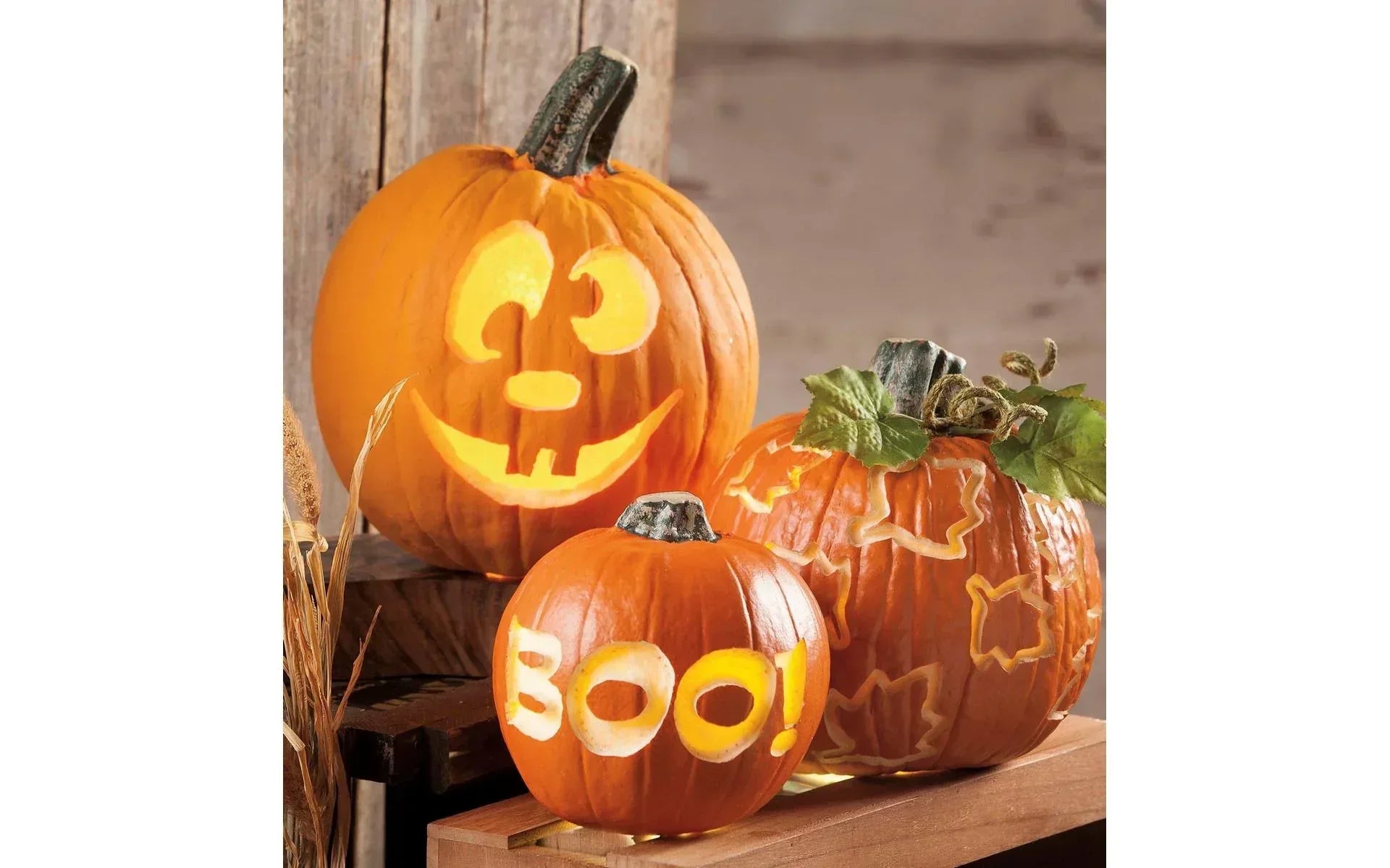 Three carved pumpkins with faces and 'BOO!' text on a wooden surface.