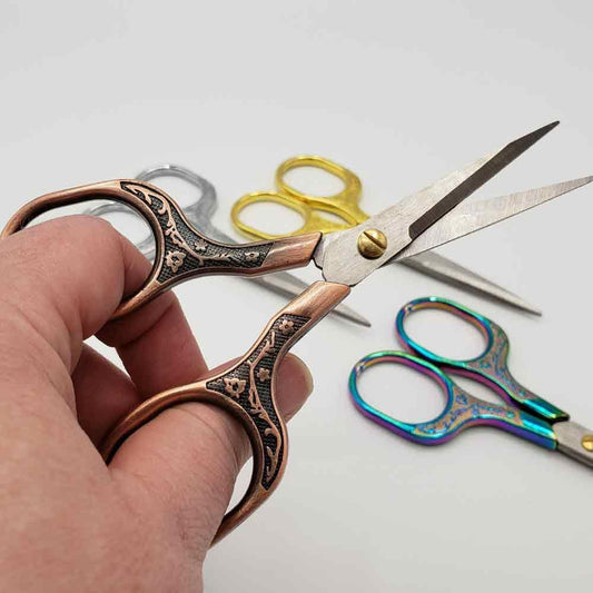 Hand holding a pair of ornate scissors with others in the background on a light gray surface